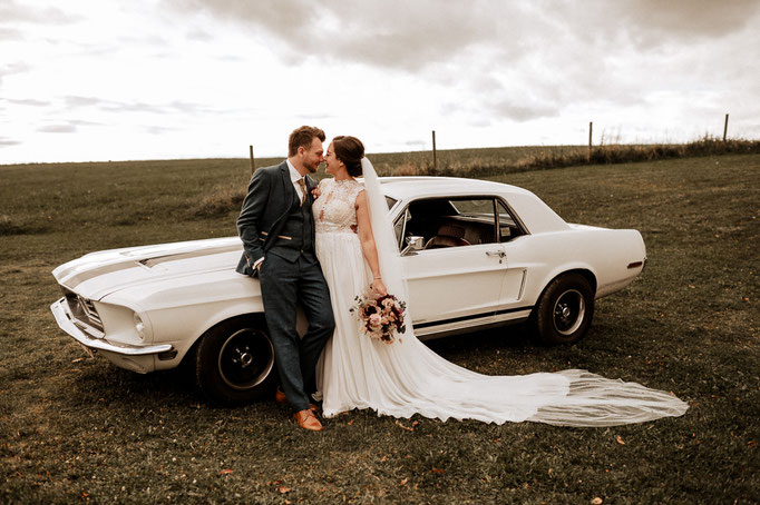 Ford Mustang als Hochzeitsauto, das Brautpaar sieht sich verliebt an. Hochzeitsfotograf ist Andreas Reiter.