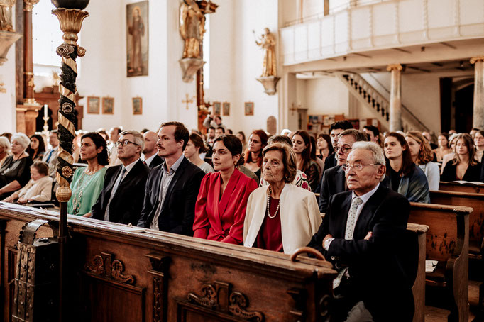 Hochzeitsfotograf in der St. Sixtus Kirche am Schliersee. Die Hochzeitsgesellschaft sitzt in den Kirchenbänken.