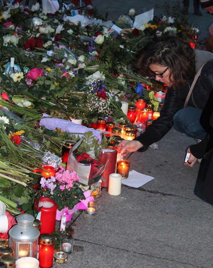 Eine Frau zündet ein Licht an vor den Blumen vor der französischen Botschaft in Berlin. Foto: Helga Karl