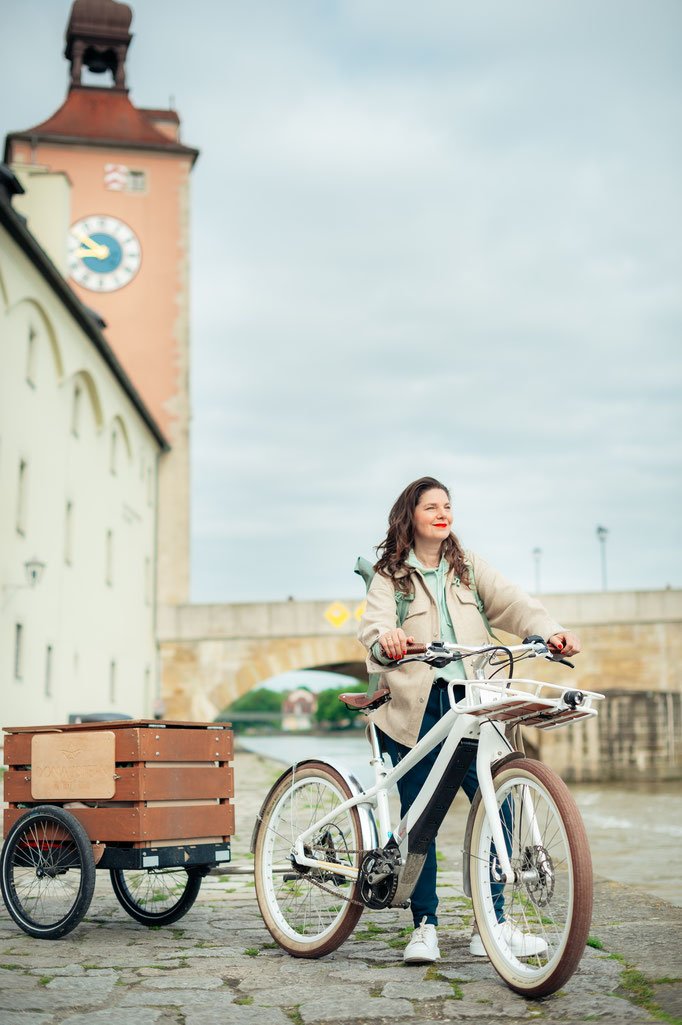 Frau mit Fahrrad vor der Steinernen Brücke in Regensburg. Business Porträt aufgenommen von Sebastian Schieder, Fotograf Regensburg.