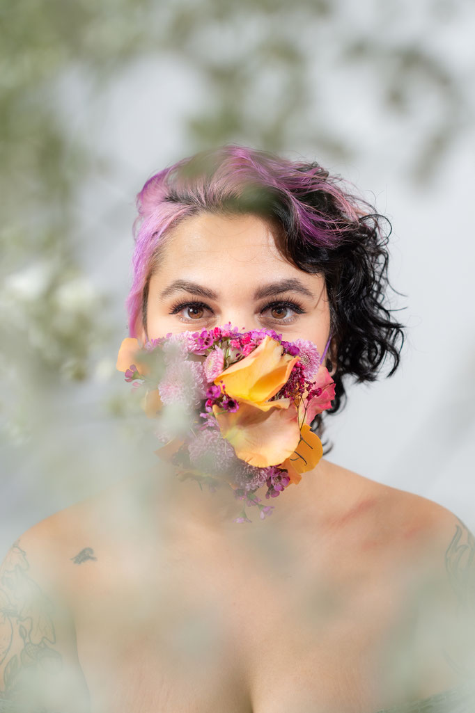 Junge Frau mir pinken Haaren und Blume vor dem Gesicht und rosa Blumenstrauss in einem Fotostudio in Regensburg.
