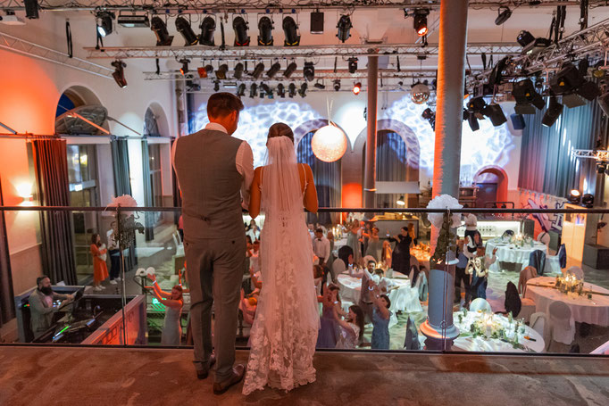 Braut und Bräutigam schauen auf die tanzende Gäste am Hochzeitstag im Maschinenhaus Markus Grein Catering