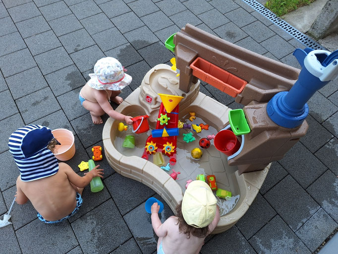 Kinder spielen und plantschen in Badehosen am Wasserspieltisch