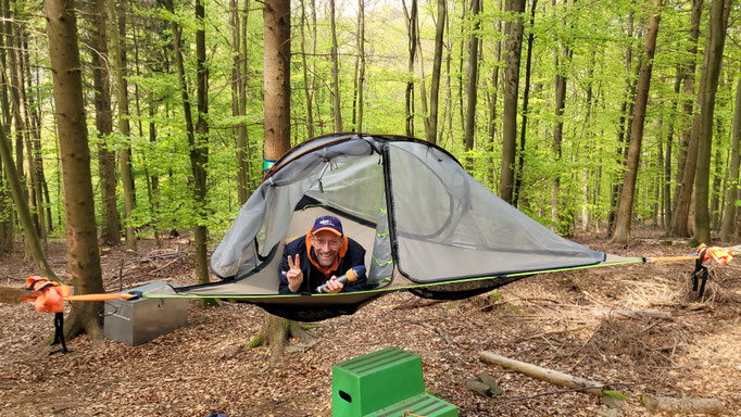 Mann mit Mikrofon liegt in einem Baumzelt im Wald