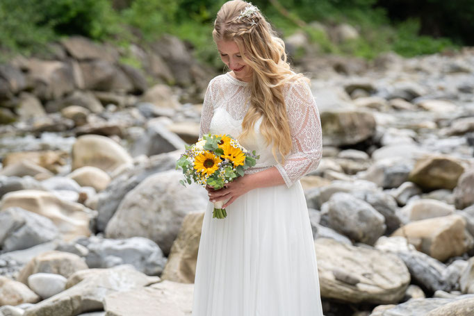 Fotografie einer Braut mit Brautstrauss auf einem von Steinen besetzten Fluss