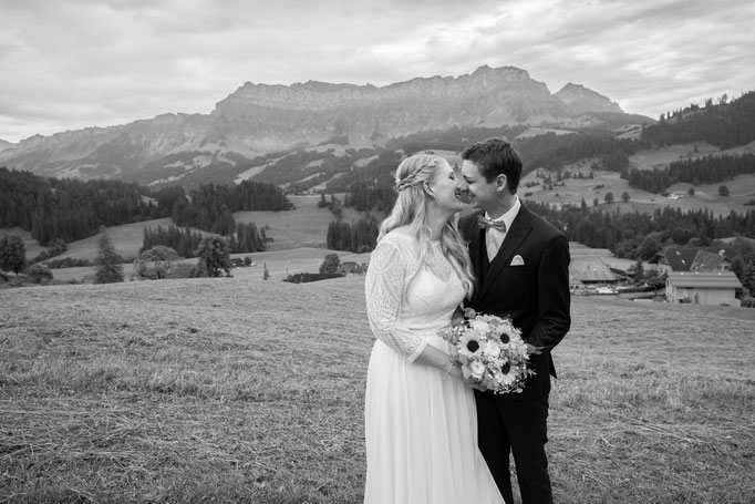 Schwarz-weiss Fotografie eines Brautpaars auf einer Wiese mit Bergen im Hintergrund