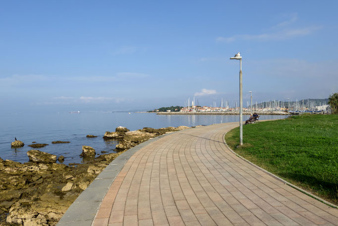 Ein breiter, gepflasterter Weg führt am Ufer und an der Marina vorbei auf die Halbinsel Isola