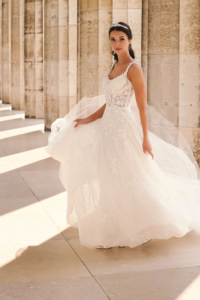 Junge Frau in einem hellen Säulengang trägt das Brautkleid Cecilia aus der Amo & Luv Kollektion