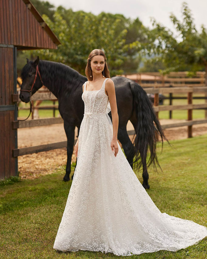 Hübsche Frau mit braunen langen Haaren trägt das Brautkleid Nusia aus der Alma Novia Kollektion 2026
