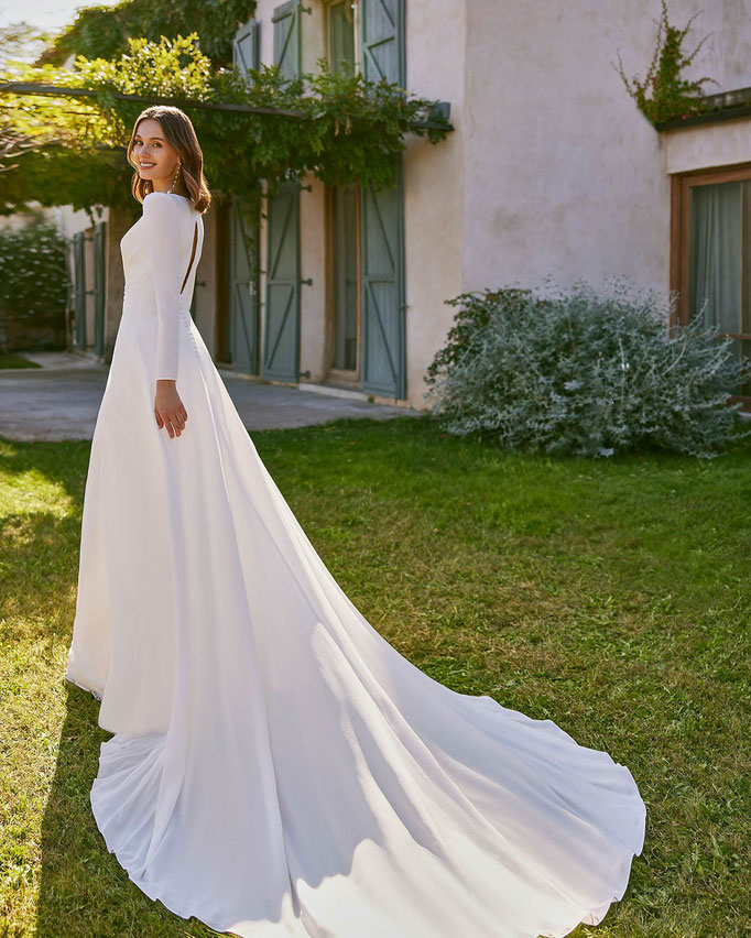 Frau mit kurzen braunen Haaren trägt das Jumpsuit-Brautkleid Naelia aus der Alma Novia Kollektion 2026