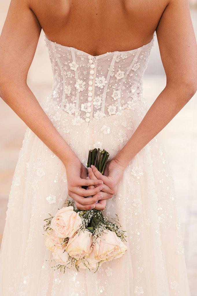Frau von hinten mit Brautstrauss trägt das Brautkleid Chelsia aus der Amo&Luv Kollektion