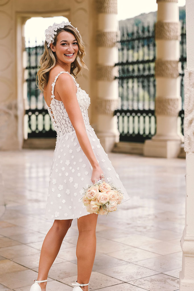 Junge blonde Frau seitlich von hinten trägt das Brautkleid Caitlin aus der Amo&Luv Kollektion