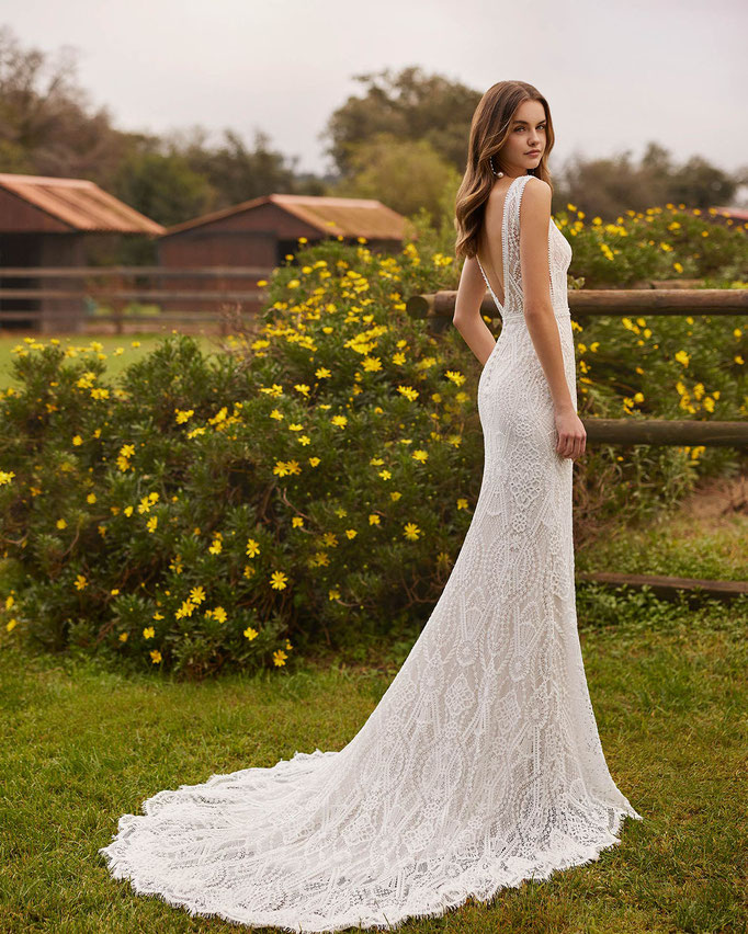 Junge Frau vor einem gelben Blumenbusch trägt das Brautkleid Numian aus der Alma Novia Kollektion 2026