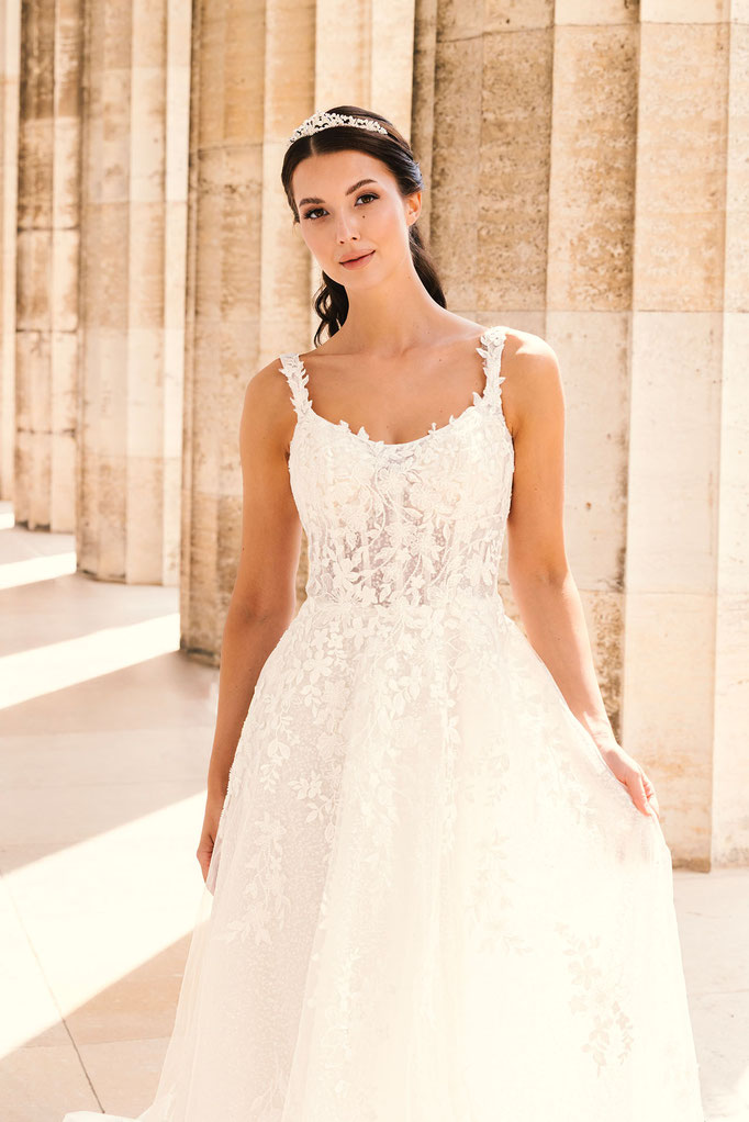 Junge Frau in einem hellen Säulengang trägt das Brautkleid Cecilia aus der Amo & Luv Kollektion