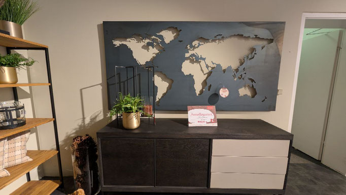 Braunes Sideboard mit hellen Schubladen, darüber eine Weltkarte aus Holz und Deko-Elemente.
