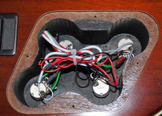 Entsprechend der 4 Regler beherbergt die Cort 4 Potentiometer. Das Fach ist mit abschirmender Farbe lackiert, um störende Einstreuungen zu unterbinden. Unter der Klappe links daneben ist eine 9V-Batterie zur Versorgung der aktiven Pickups untergebracht.