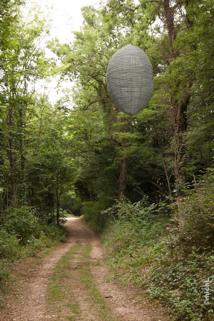 sculpture en acier en forme de cocon suspendu dans la forêt