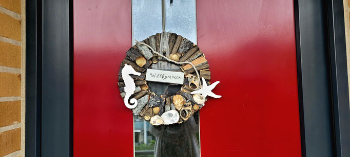 Weiß-grauer maritim dekorierter Holzkranz an roter Haustür.