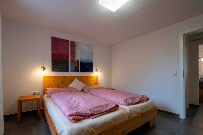 Doppelbett mit rotkarierter Bettwäsche, Nachttischlampen und schönem Bild über dem Kopfende