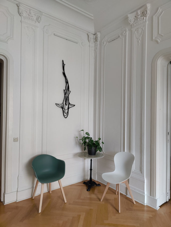 Waiting area at Doumit Dental Practice Berlin-Friedenau with two chairs, a table, and wall art of a stylised shark.