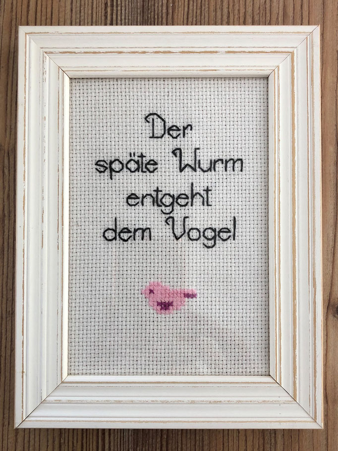 Stickbild mit Spruch im Holzrahmen hinter Glas - schwarze Schrift, kleiner rosa Vogel - Der späte Wurm entgeht dem Vogel - Statement-Stickerei - Stickspruch