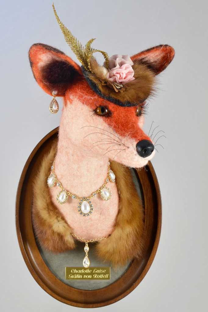 Trophenkopf eines Fuchses aus Rot-weißem Fell. Der Tierkopf ist mit einem Hut, edlem Schmuck und Pelz dekoriert.