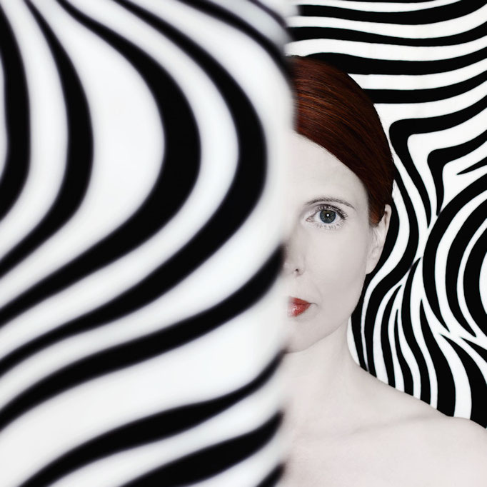 Manuela Deigert Bildsprache, psychedelisches halbes Selbstportrait zwischen schwarz weiss gemusterten Vorder-und Hintergrund