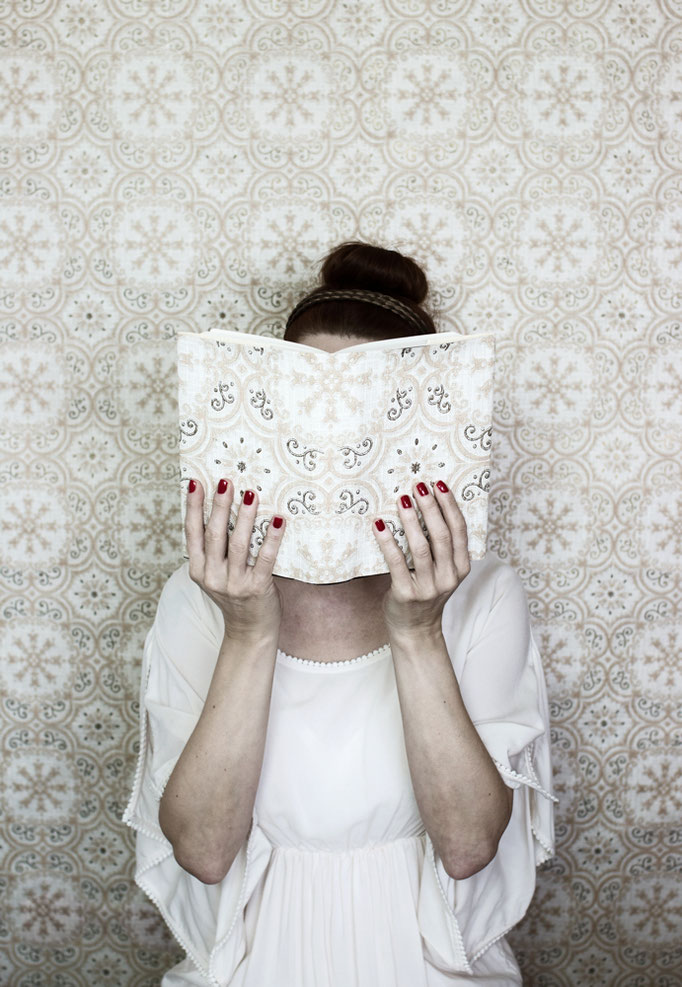 Manuela Deigert Bildsprache Selbstportrait mit gemustertem Buch in meinen Händen vor dem Gesicht und im Hintergrund dasselbe Muster in der Tapete