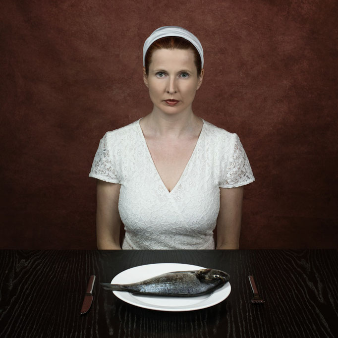 Manuela Deigert Projekte Friday is fishday, farbiges Selbstportrait an einem Tisch sitzend mit einem Teller auf dem eine rohe Dorade liegt