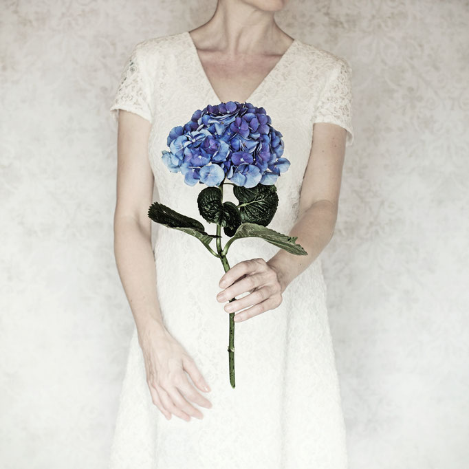 Manuela Deigert Bildsprache Selbstportrait mit weissem Kleid und blauer Hortensie in einer Hand