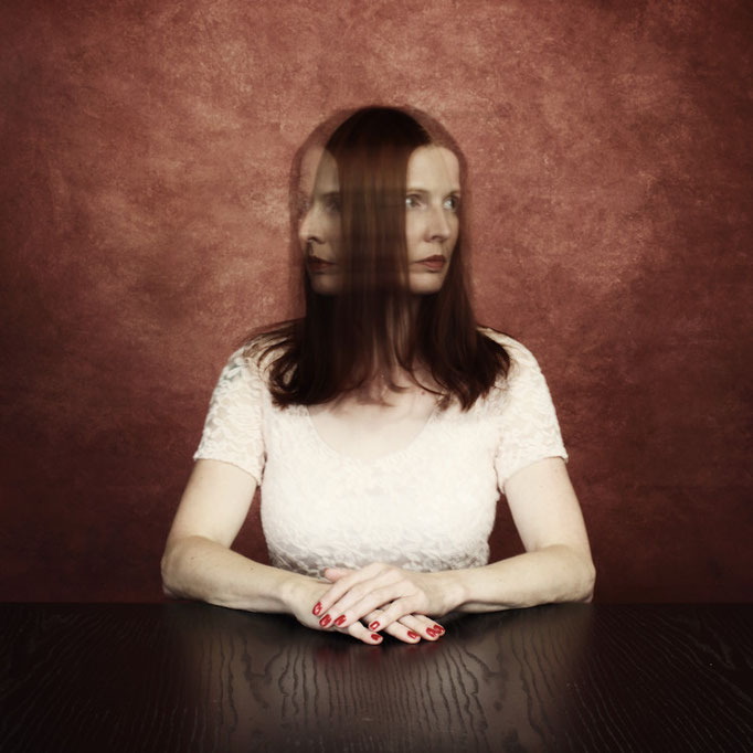 Manuela Deigert Bildsprache, dynamisches Selbstportrait am Tisch mit unscharfem Kopf, der sich nach rechts und links dreht