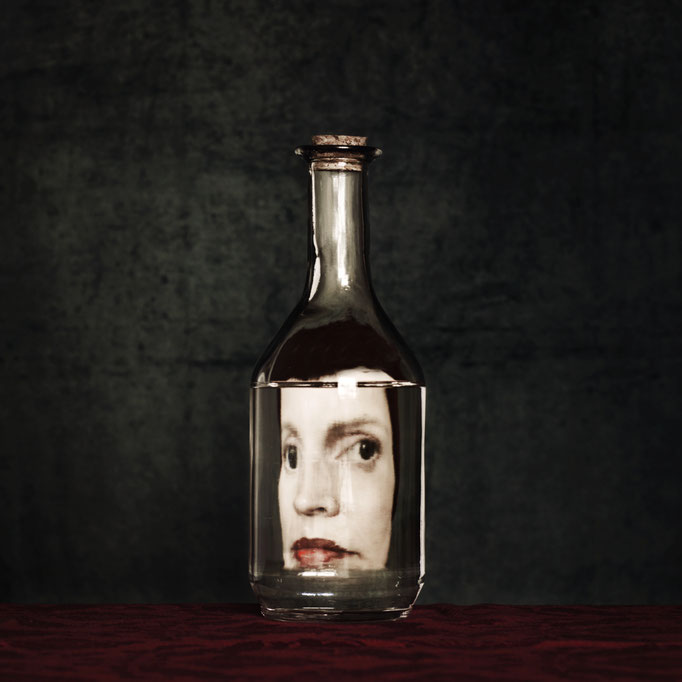 Manuela Deigert Bildsprache Selbstportrait als Reflexion in einer Glasflasche mit dunkelgrünen Hintergrund