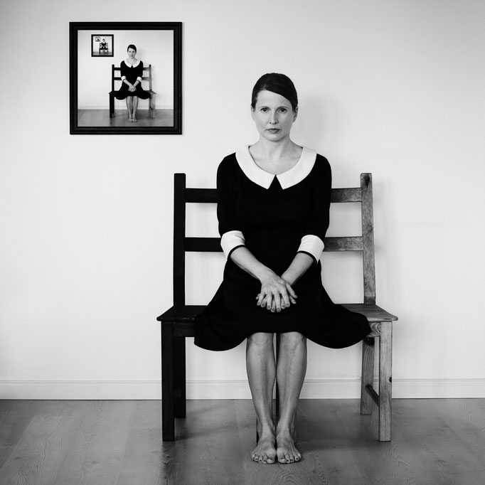Manuela Deigert Bildsprache Selbstportrait in einem Kleid auf einem Stuhl sitzend mit einem Bild von mir an der Wand in der selben Position