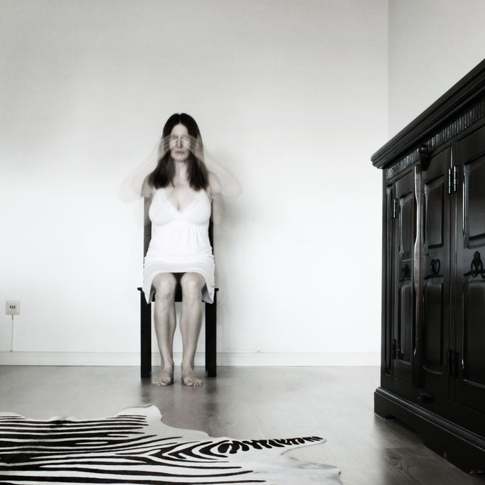 Manuela Deigert Bildsprache Langzeitbelichtetes Selbstportrait sitzend in einem Raum mit Bewegung der Hände vor dem Mund, Ohren und Augen