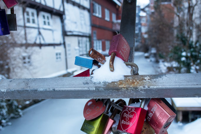 Schlösser mit eingeritzten Namen hängen am Geländer einer Brücke. Auf den Schlössern liegt Schnee.