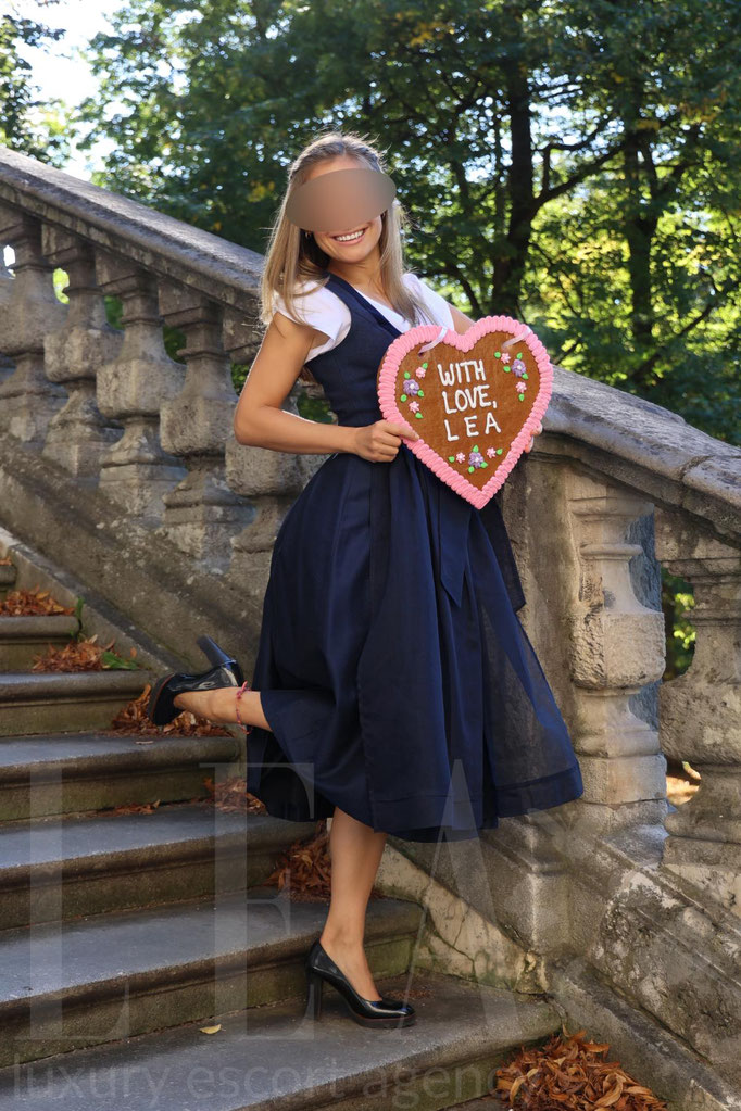 Escort Ella mit Herz-Lebkuchen im Dirndl – charmante High Class Begleitung für das Oktoberfest in München