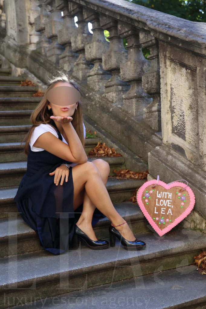 Escort Lady Ella sitzt im Dirndl auf einer Treppe – exklusive Wiesn Begleiterin in München