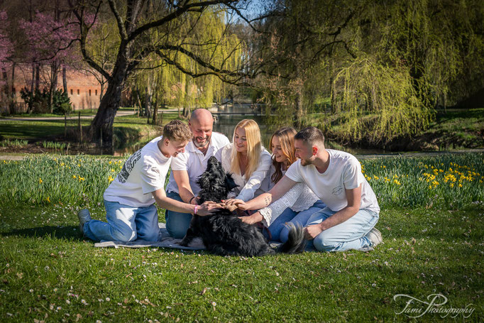 Familienshooting mit Hund in Ulm – Familie sitzt im Gras und streichelt ihren Hund im Park Glacis