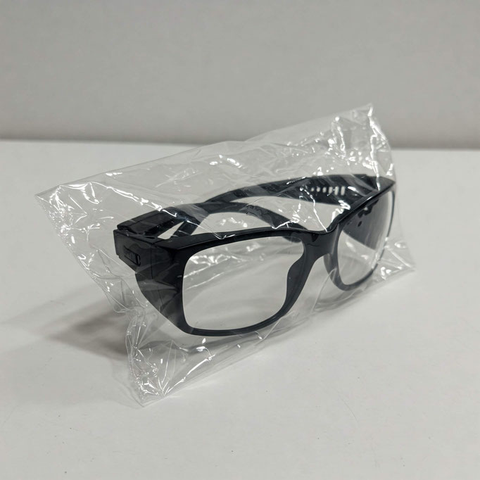 Encima de una mesa blanca con un fondo blanco hay unos lentes de protección que están empacados dentro de una bolsa de celofán transparente de 15x25 con adhesivo