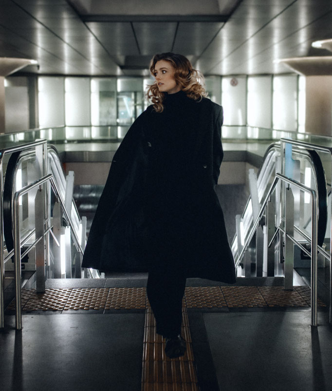 blonde frau mit locken und langem mantel auf rolltreppe ubahn