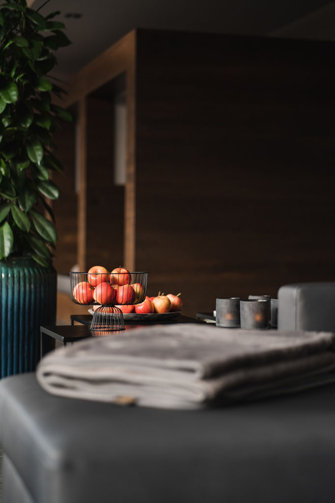 Liebevoll arrangierte Äpfel, Kerzen und eine weiche Decke im stilvollen Loungebereich des Hotel Mair am Ort Living in Partschins bei Meran in Südtirol. Die dekorativen Details schaffen eine warme und einladende Wohlfühlatmosphäre.
