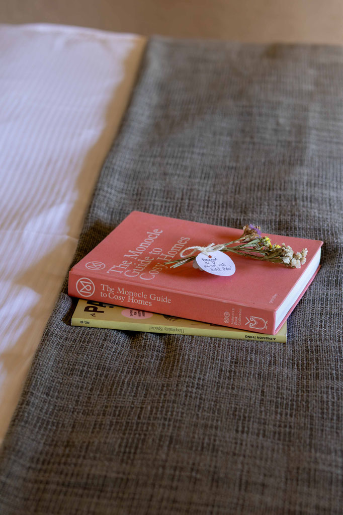 Bücher und ein kleiner Trockenblumenstrauß als liebevolle Dekoration auf einem Bett im Boutiquehotel PETRUS in Reischach-Bruneck • Südtirol, die eine gemütliche und stilvolle Atmosphäre schaffen.