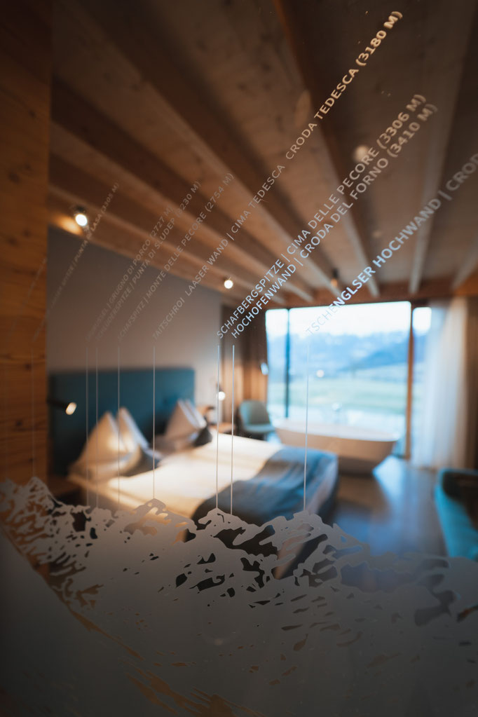A view through a labelled glass pane of a modern hotel room with a panoramic mountain view.
