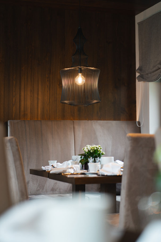 Stilvoll gedeckter Tisch im Restaurant des Hotel Mair am Ort Living in Partschins bei Meran in Südtirol mit gemütlicher Sitzbank, dekorativen Blumen und moderner Pendelleuchte. Das warme Ambiente lädt zu einem entspannten Frühstück oder Abendessen ein.