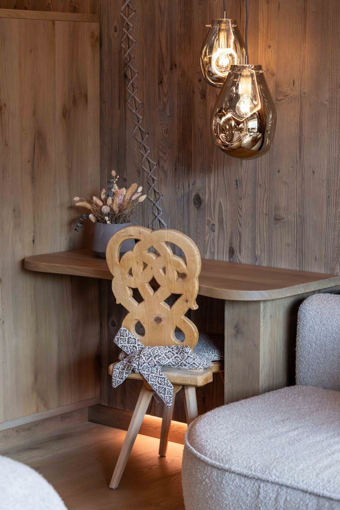 Gemütliche Sitzecke mit traditionellem Holzstuhl, warmen Pendelleuchten und natürlichen Materialien im DER ENGEL im Tannheimertal. Liebevolle Details und alpines Design schaffen eine behagliche Wohlfühlatmosphäre.