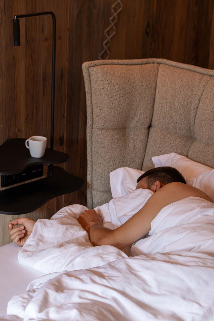 Gast entspannt in einem gemütlichen Hotelbett im DER ENGEL im Tannheimertal. Warme Holzelemente, weiche Bettwäsche und stilvolles Design schaffen eine behagliche Atmosphäre für erholsame Nächte.