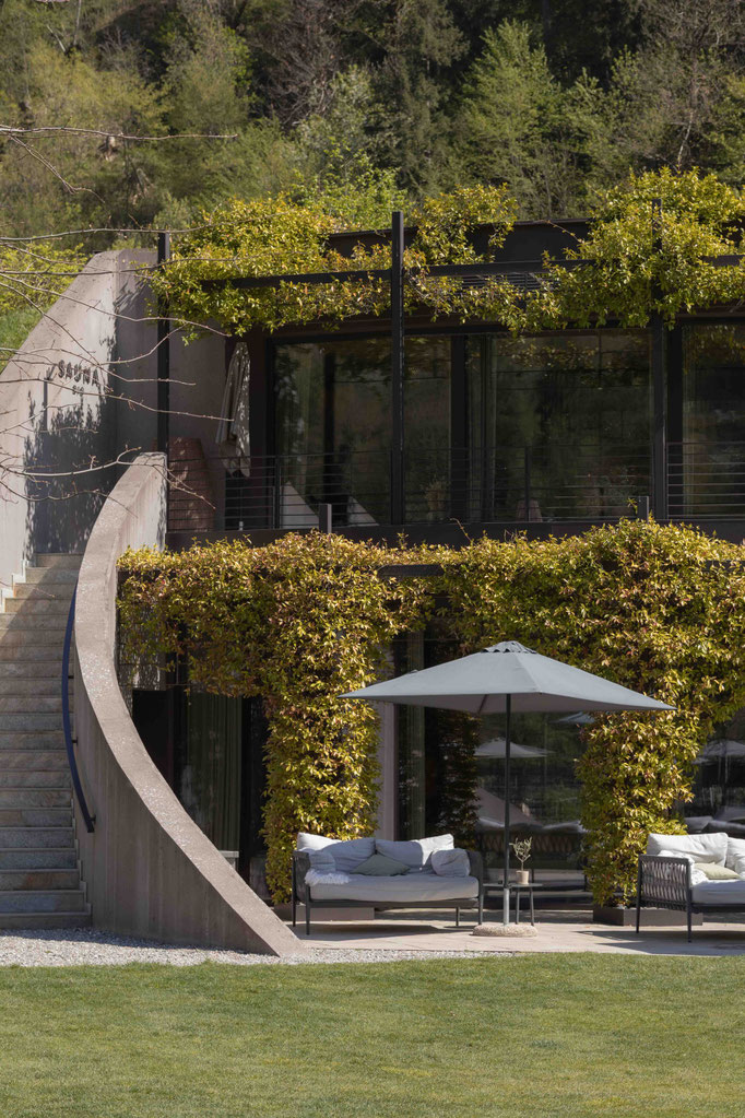 Begrünte Architektur des Apfelhotels mit modernen Glasfronten, geschwungener Treppe und stilvollem Loungebereich im Garten.