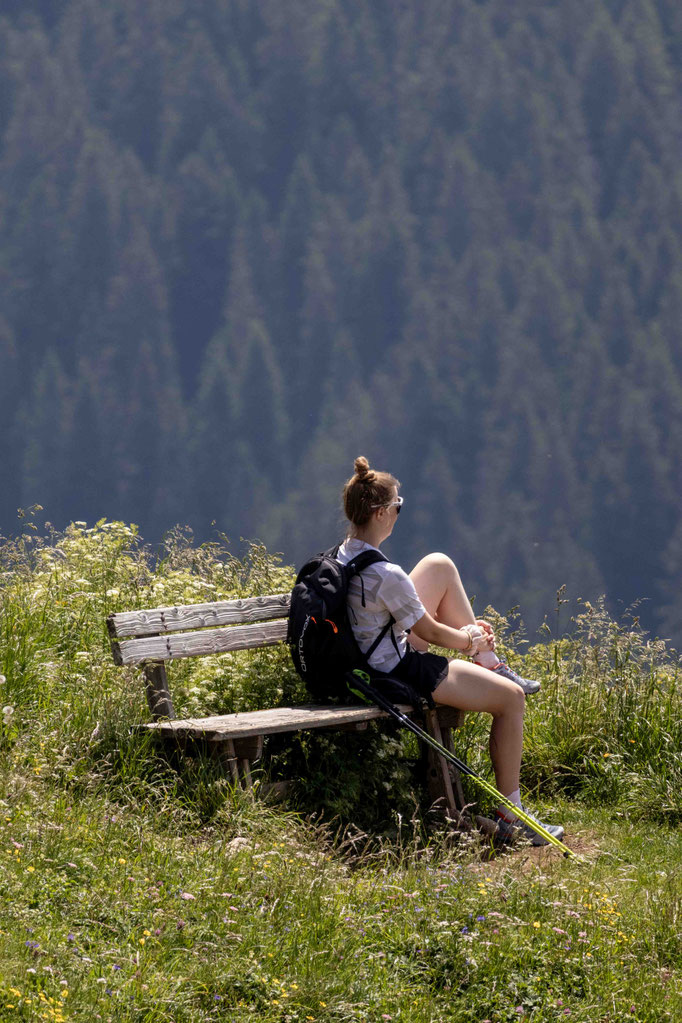 Eine Wanderin genießt auf einer Bank den Blick über die eindrucksvolle Berglandschaft des Tannheimertals. Rund um DER ENGEL im Tannheimertal laden zahlreiche Panoramawege dazu ein, innezuhalten, die Natur zu genießen und neue Energie in den Allgäuer Alpen