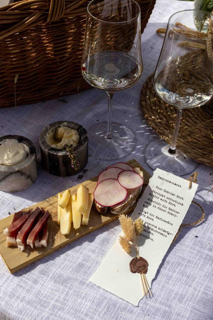 A lovingly prepared regional snack of cheese, bacon, radish bread and wine on the terrace of the PETRUS boutique hotel in Reischach-Bruneck • South Tyrol, where you can experience South Tyrolean culinary delights and hospitality.