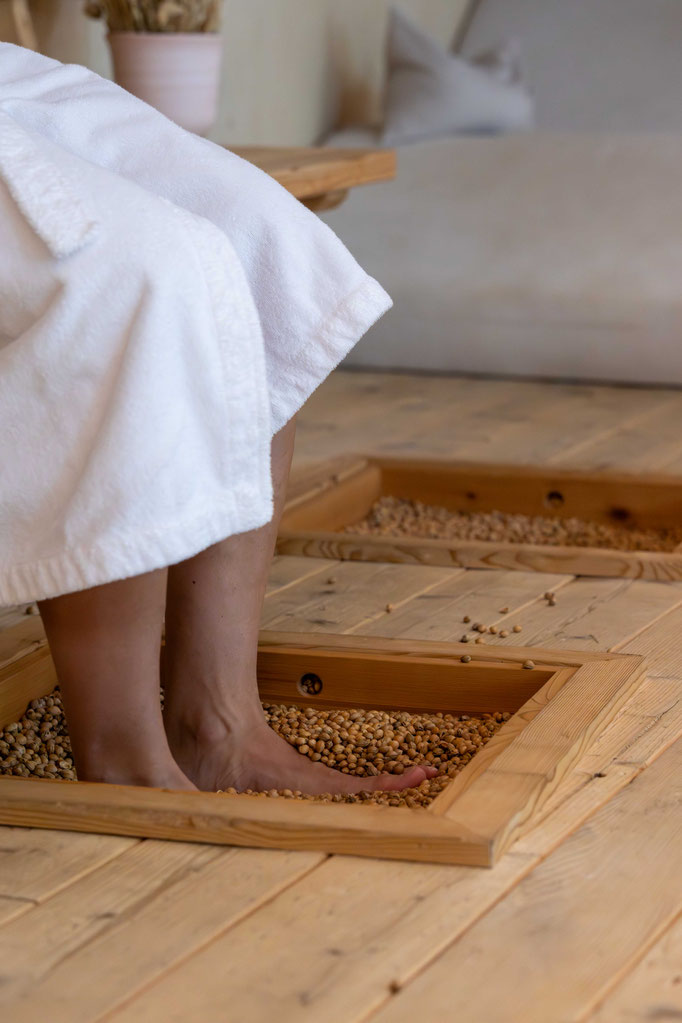 A guest, carrying a towel, walks barefoot along the Kneipp and barefoot trail in the wellness area of the PETRUS Boutique Hotel in Reischach-Bruneck • South Tyrol, naturally promoting relaxation and well-being.